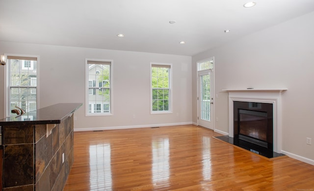 unfurnished living room with baseboards, recessed lighting, a glass covered fireplace, and light wood-type flooring