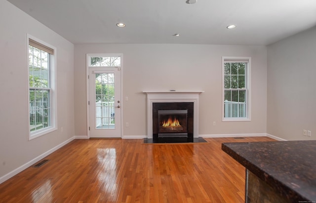 unfurnished living room featuring baseboards, a fireplace with flush hearth, visible vents, and hardwood / wood-style flooring