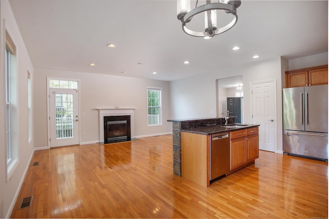kitchen with light wood-style floors, stainless steel appliances, brown cabinets, and a notable chandelier