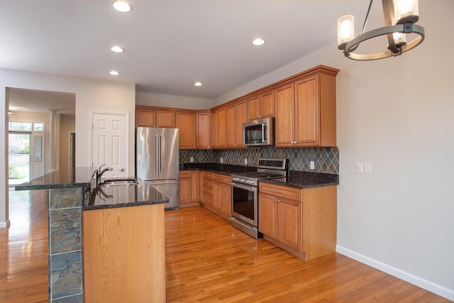 kitchen featuring a sink, stainless steel appliances, backsplash, and light wood-style flooring