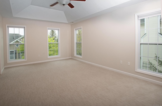 empty room featuring light carpet, baseboards, a raised ceiling, and ceiling fan