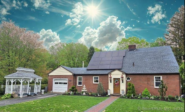 view of front of property featuring an attached garage, a gazebo, roof mounted solar panels, a front lawn, and asphalt driveway
