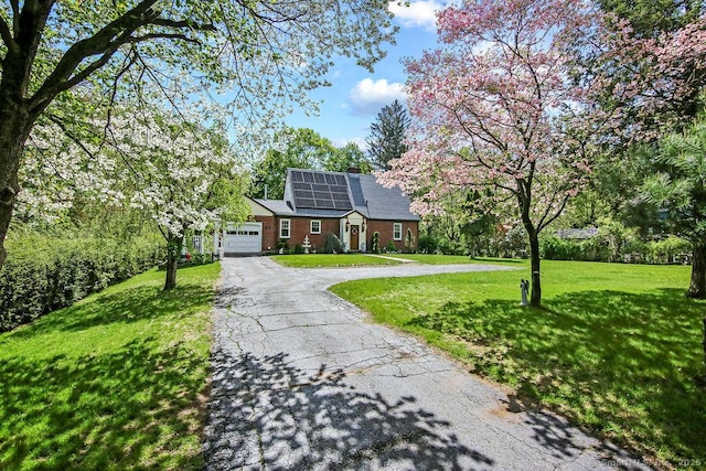 view of front of property with asphalt driveway, a garage, solar panels, a front lawn, and a chimney