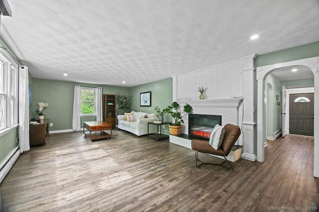living area featuring wood finished floors, arched walkways, a brick fireplace, a baseboard heating unit, and baseboards