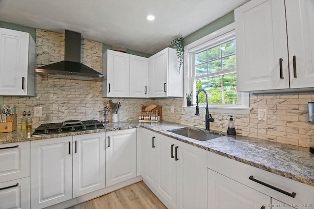 kitchen with wall chimney range hood, gas stovetop, a sink, light wood-type flooring, and light stone countertops