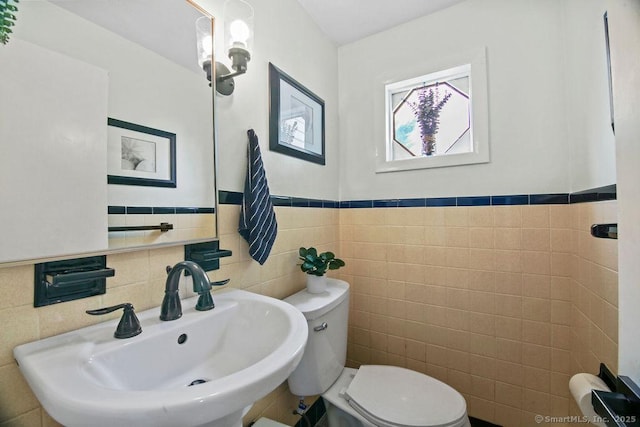 bathroom featuring toilet, tile walls, a sink, and a wainscoted wall