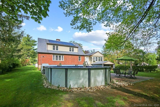 back of house featuring roof mounted solar panels, an outdoor pool, a lawn, a chimney, and a patio area
