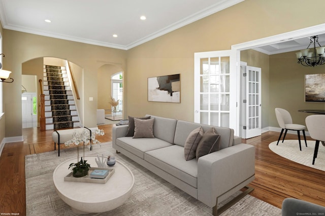 living area with arched walkways, a chandelier, stairway, wood finished floors, and ornamental molding