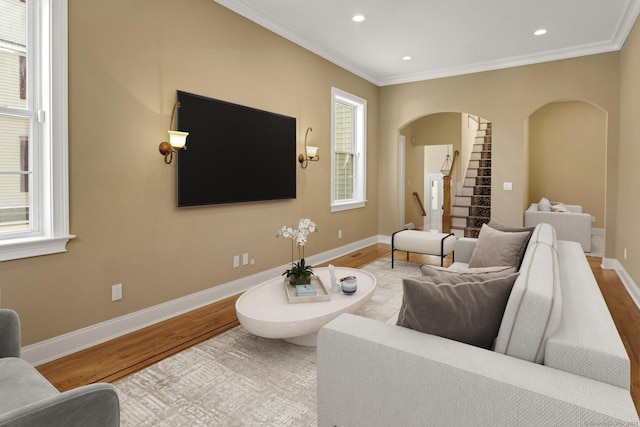 living area with arched walkways, stairs, wood finished floors, ornamental molding, and baseboards