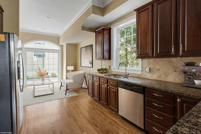 kitchen with stainless steel appliances, a sink, wood finished floors, dark stone counters, and crown molding