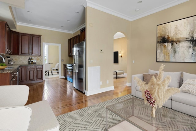 living area featuring arched walkways, light wood-style flooring, crown molding, and baseboards