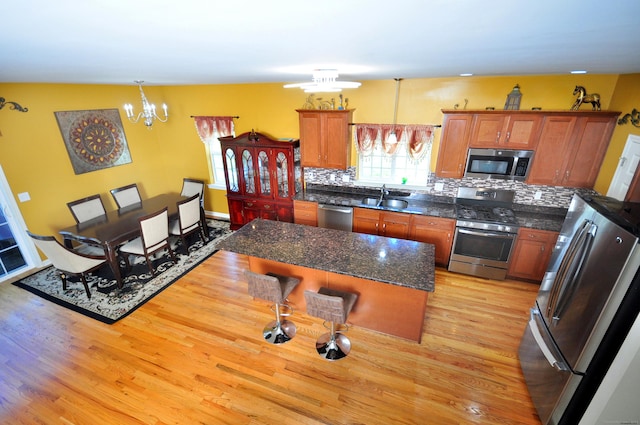 kitchen with stainless steel appliances, a sink, a chandelier, light wood finished floors, and brown cabinetry