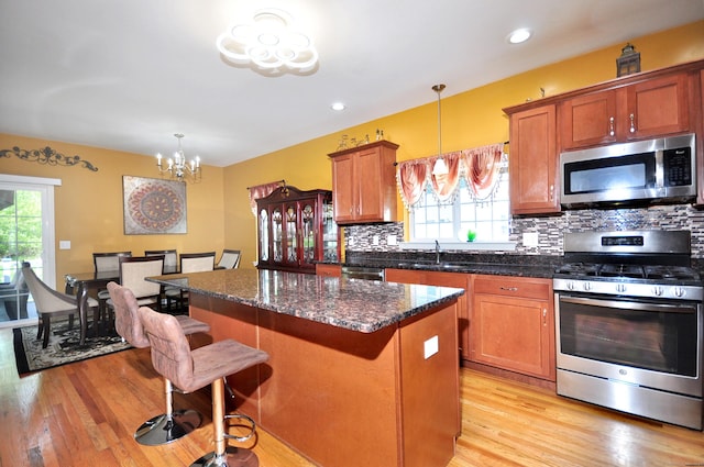 kitchen with appliances with stainless steel finishes, a sink, backsplash, a chandelier, and light wood finished floors