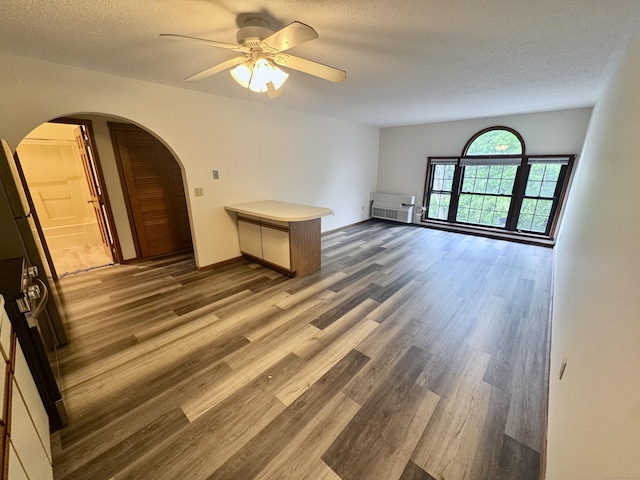 unfurnished living room with wood finished floors, a textured ceiling, arched walkways, a ceiling fan, and baseboards