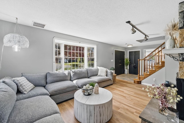 living area featuring rail lighting, stairs, light wood finished floors, and visible vents