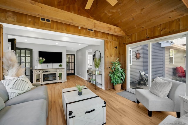 living room featuring light wood-type flooring, wood walls, baseboards, visible vents, and lofted ceiling