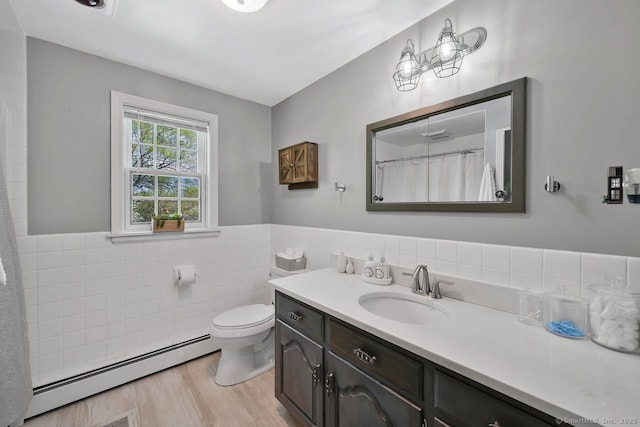 bathroom featuring tile walls, a baseboard heating unit, toilet, wainscoting, and vanity