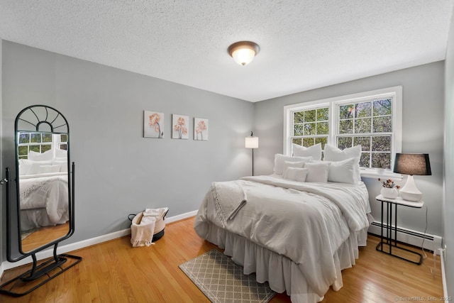 bedroom featuring a textured ceiling, baseboards, baseboard heating, and wood finished floors