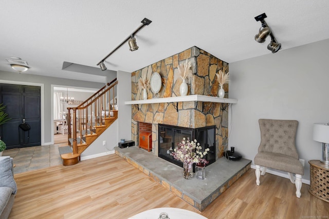 living room with rail lighting, a fireplace, an inviting chandelier, and wood finished floors