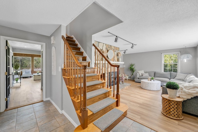 staircase with rail lighting, baseboards, tile patterned floors, and a textured ceiling