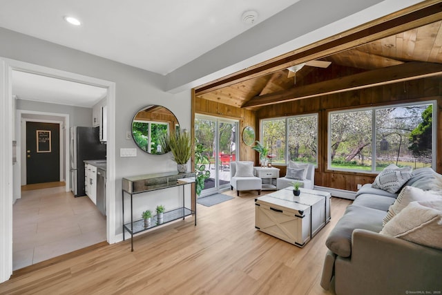 living area with vaulted ceiling, a baseboard radiator, wooden walls, baseboards, and light wood-style floors