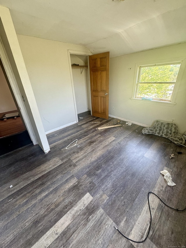 unfurnished bedroom featuring baseboards, dark wood-style flooring, lofted ceiling, and a closet
