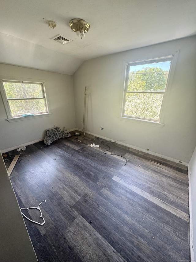 interior space with baseboards, vaulted ceiling, wood finished floors, and visible vents