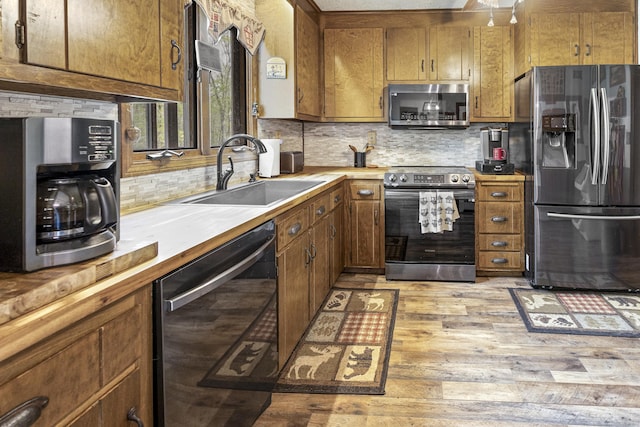 kitchen featuring a sink, stainless steel appliances, brown cabinetry, light wood-type flooring, and tasteful backsplash