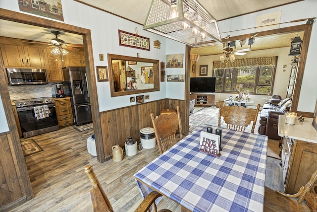 dining space featuring wainscoting, ceiling fan, wooden walls, and light wood-type flooring