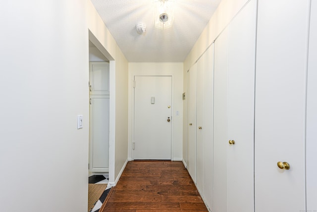 corridor with dark wood-style floors, baseboards, and a textured ceiling