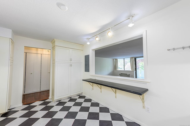 hallway with dark flooring, electric panel, rail lighting, a textured ceiling, and baseboards
