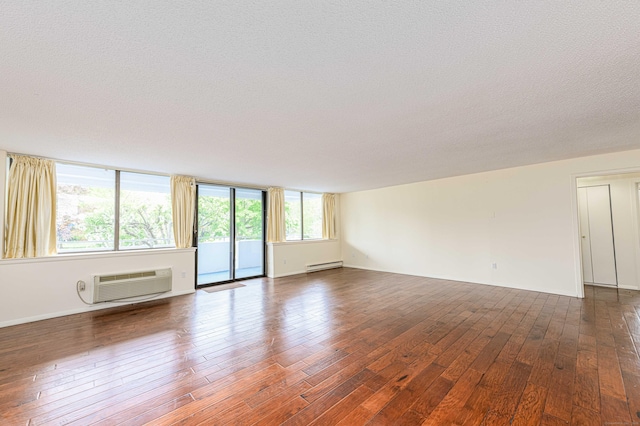 unfurnished room featuring a baseboard heating unit, a wall unit AC, hardwood / wood-style floors, a textured ceiling, and baseboards