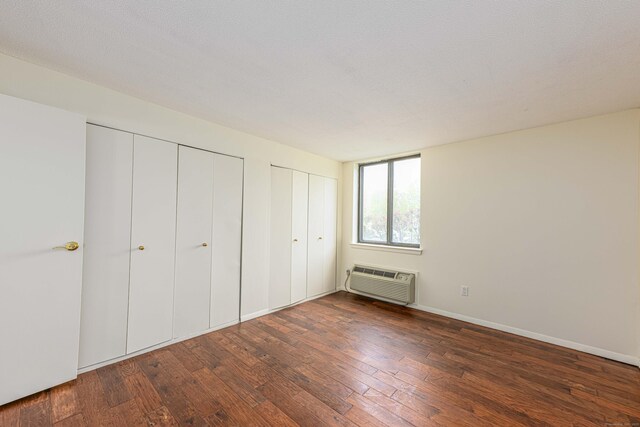 unfurnished bedroom featuring a wall mounted AC, wood-type flooring, two closets, and baseboards