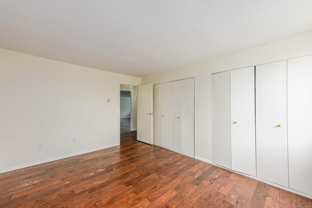 unfurnished bedroom featuring multiple closets, wood finished floors, and baseboards
