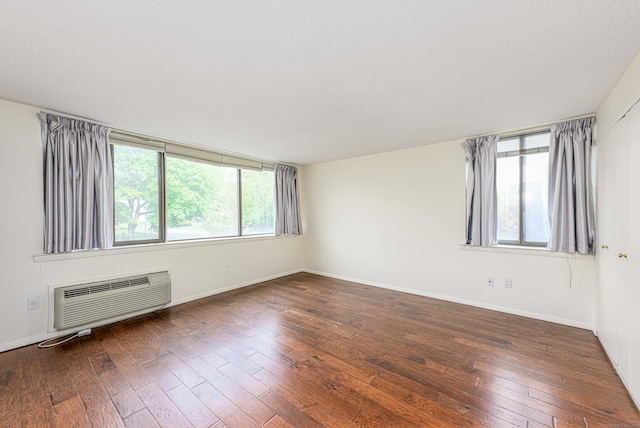 empty room with a wall unit AC, hardwood / wood-style flooring, baseboards, and a textured ceiling