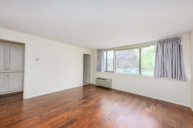 unfurnished room with an AC wall unit, wood-type flooring, baseboards, and a textured ceiling