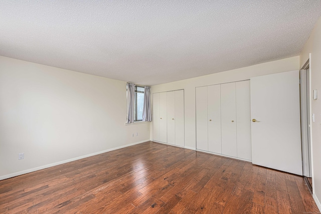 unfurnished bedroom featuring multiple closets, wood-type flooring, a textured ceiling, and baseboards
