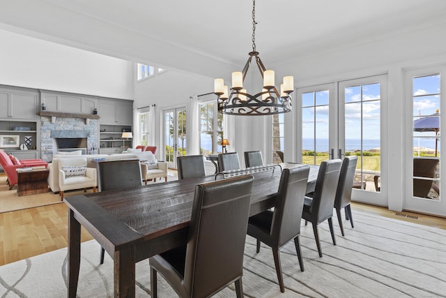 250 Joshua Point Rd, Guilford, CT 06437 - dining space featuring a chandelier, light wood-style flooring, a stone fireplace, a water view, and a towering ceiling