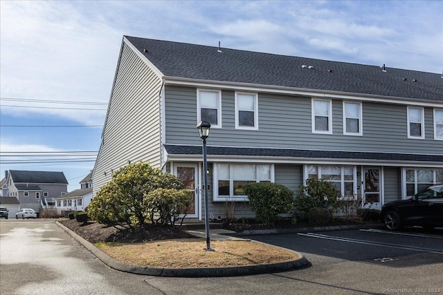 view of property with uncovered parking and roof with shingles