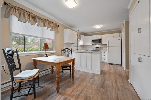 kitchen with appliances with stainless steel finishes, ornamental molding, white cabinetry, wood finished floors, and decorative backsplash