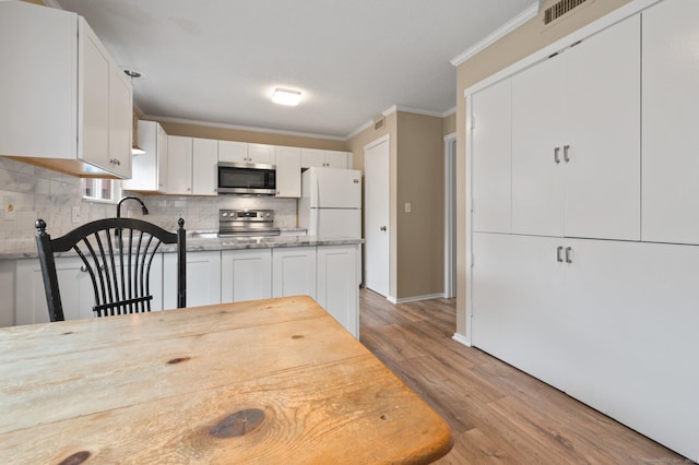 kitchen featuring appliances with stainless steel finishes, light wood finished floors, tasteful backsplash, ornamental molding, and white cabinets