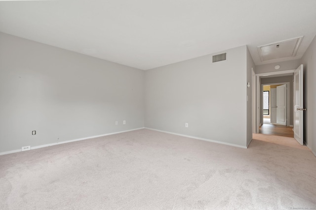 empty room with attic access, light carpet, and baseboards