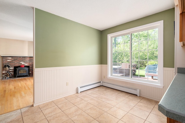 empty room featuring a wainscoted wall, a wood stove, light tile patterned flooring, and a baseboard radiator
