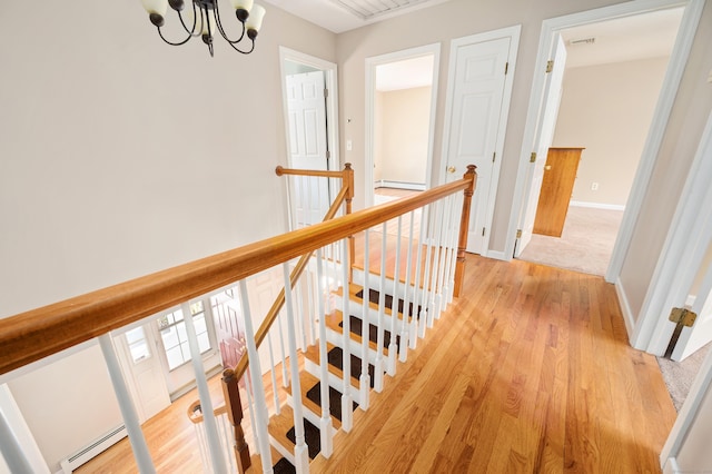 hallway with baseboard heating, an upstairs landing, light wood-style floors, and a chandelier