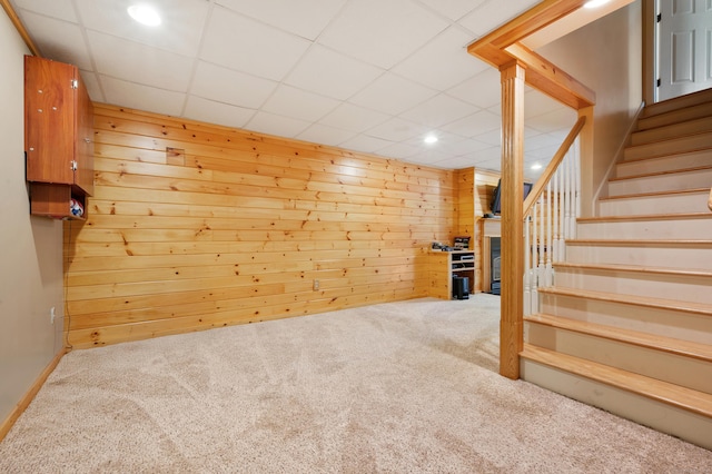 finished basement with carpet, recessed lighting, stairway, a drop ceiling, and wood walls