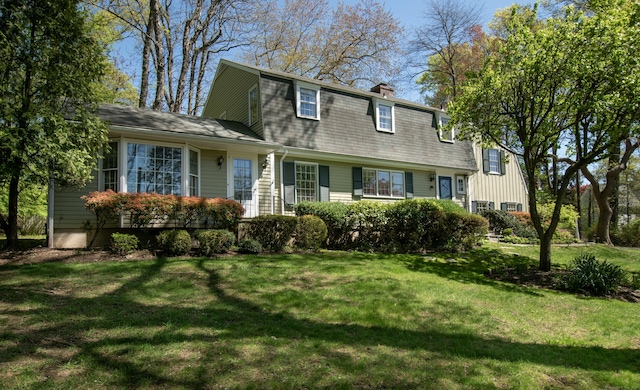 view of front facade featuring a gambrel roof, a front yard, and a chimney