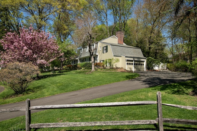 view of side of home with a gambrel roof, asphalt driveway, a chimney, and an attached garage