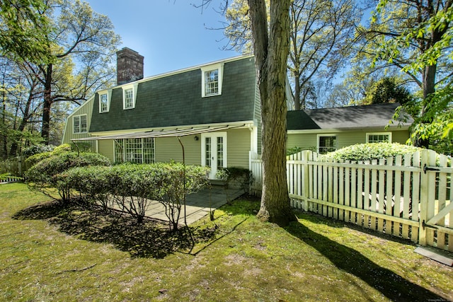 back of house with a chimney, a patio, roof with shingles, and a gambrel roof