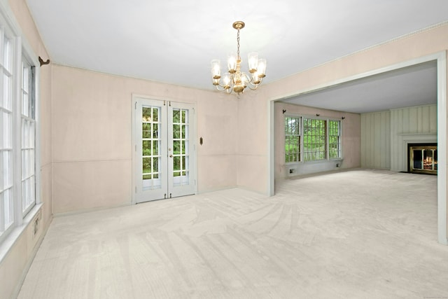 unfurnished dining area featuring carpet flooring, a chandelier, french doors, and a glass covered fireplace