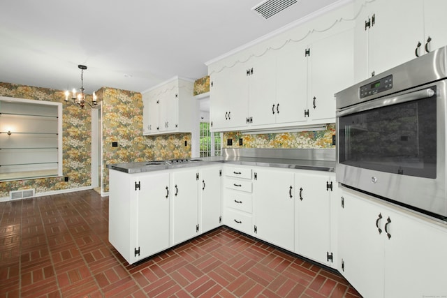 kitchen featuring stainless steel counters, brick patterned floors, oven, a chandelier, and wallpapered walls